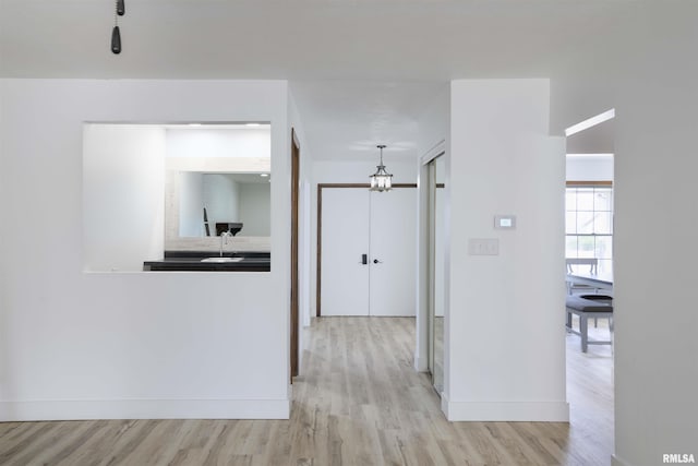 hall featuring a sink, light wood-style flooring, and baseboards