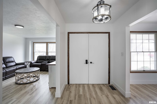 entryway with visible vents, a textured ceiling, a chandelier, light wood-type flooring, and baseboards