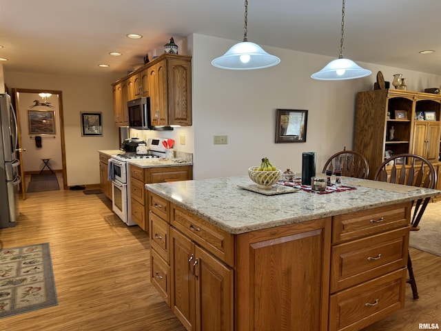 kitchen with light wood-type flooring, light stone counters, decorative light fixtures, double oven range, and a kitchen island