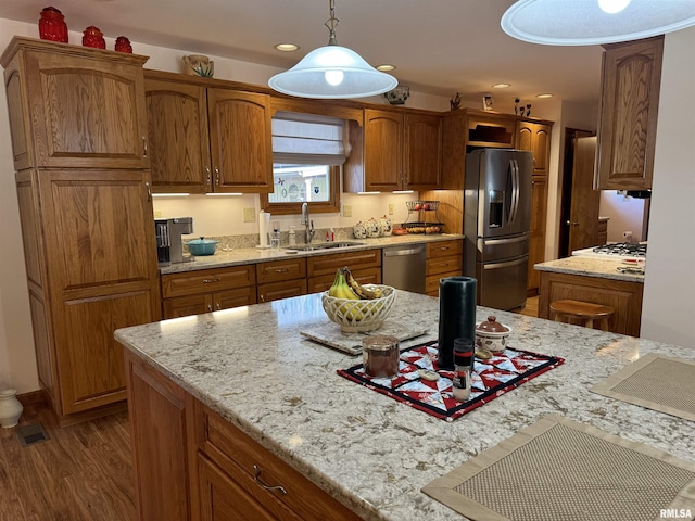 kitchen featuring sink, stainless steel appliances, light stone counters, decorative light fixtures, and hardwood / wood-style flooring