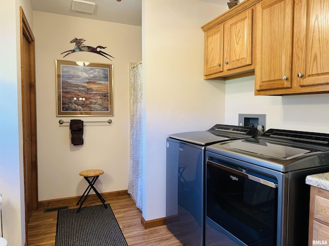 laundry room featuring washing machine and clothes dryer, cabinets, and light wood-type flooring