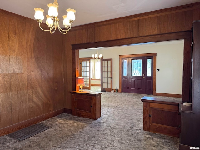 foyer entrance with dark colored carpet, wooden walls, plenty of natural light, and a notable chandelier