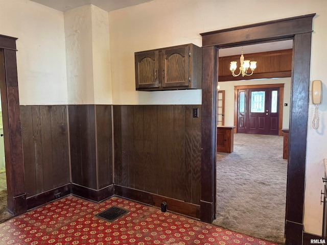 kitchen featuring wood walls, an inviting chandelier, hanging light fixtures, dark brown cabinets, and light colored carpet