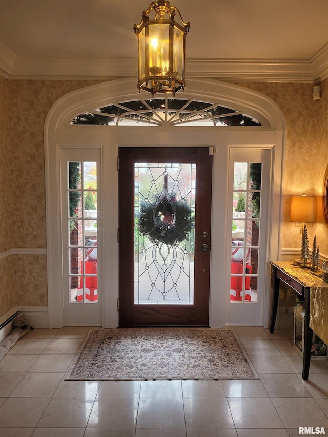 tiled foyer entrance featuring plenty of natural light, ornamental molding, and a notable chandelier