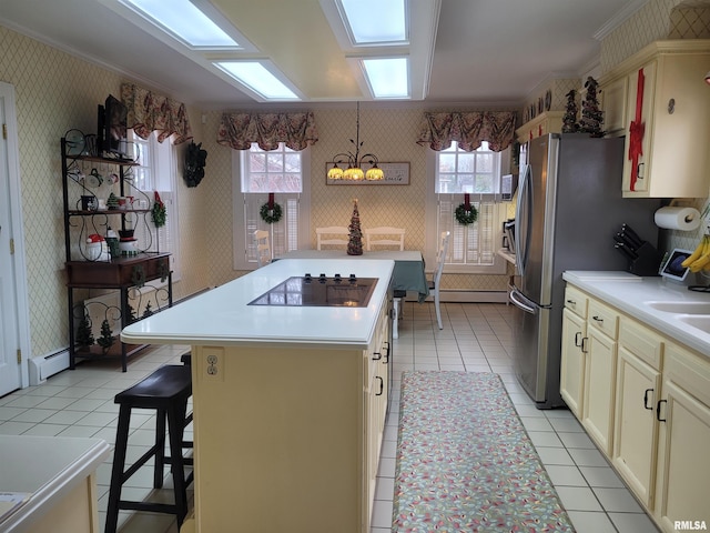 kitchen with a center island, cream cabinets, black electric stovetop, hanging light fixtures, and a breakfast bar area