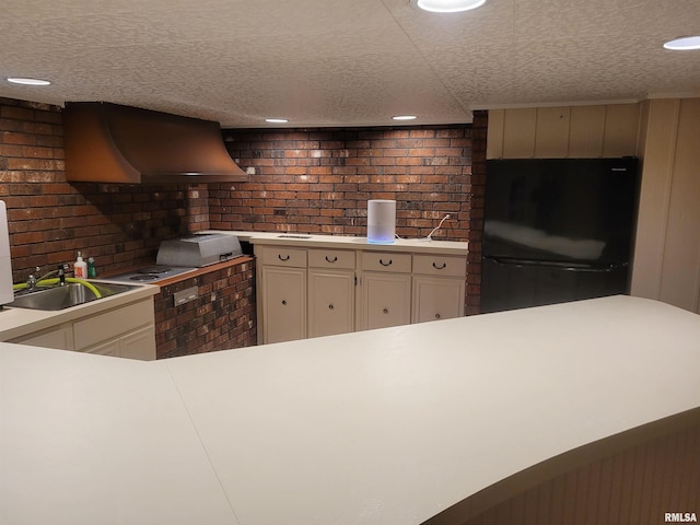 kitchen with black refrigerator, wall chimney exhaust hood, brick wall, a textured ceiling, and sink