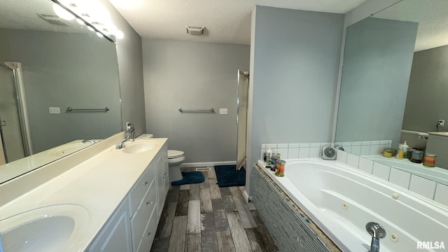 bathroom featuring vanity, a textured ceiling, tiled tub, hardwood / wood-style flooring, and toilet