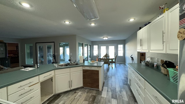 kitchen with white cabinets, sink, a textured ceiling, dishwashing machine, and light hardwood / wood-style floors