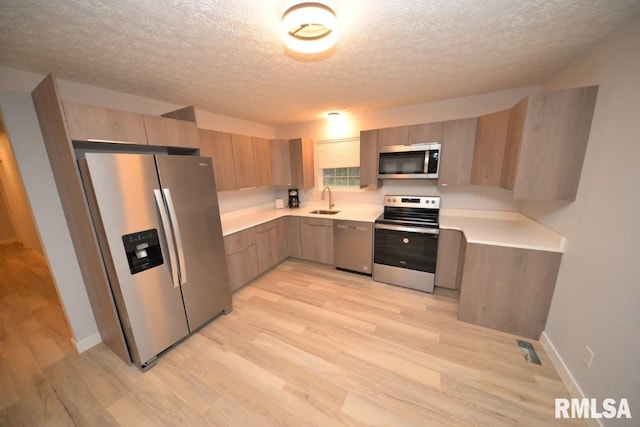 kitchen with a textured ceiling, light wood-type flooring, stainless steel appliances, and sink