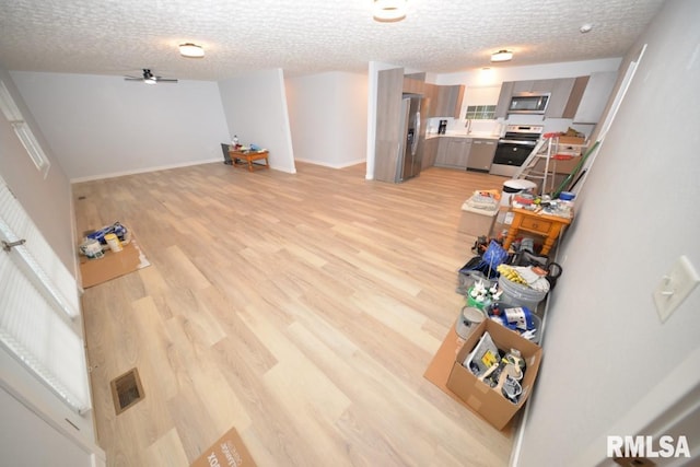 living room with a textured ceiling, light hardwood / wood-style flooring, ceiling fan, and sink