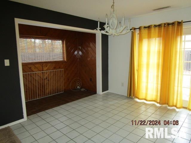 unfurnished dining area with light tile patterned floors, wooden walls, and a notable chandelier