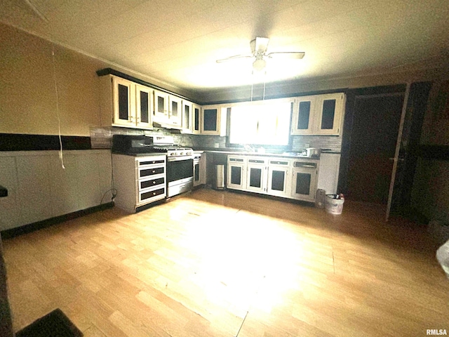 kitchen with white cabinets, light hardwood / wood-style flooring, gas range, ceiling fan, and tasteful backsplash