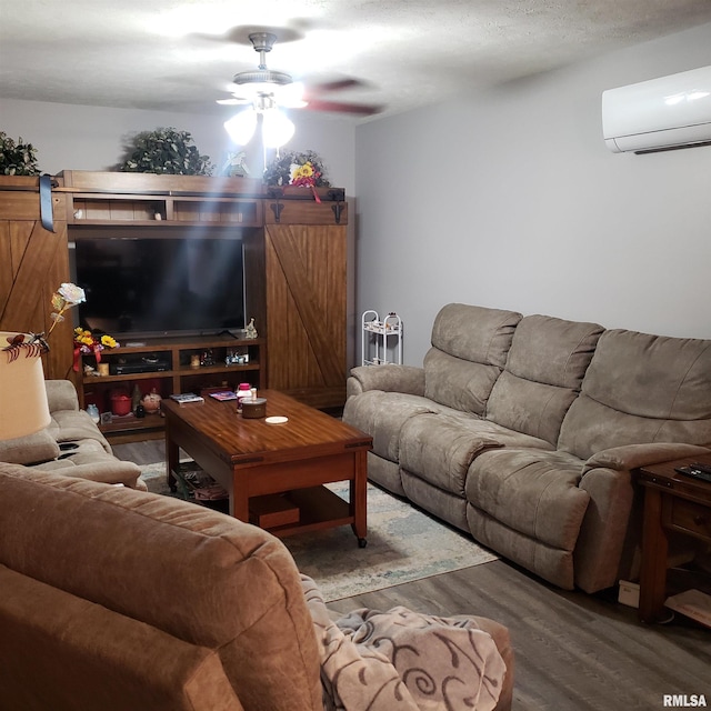 living room with a textured ceiling, a wall mounted AC, dark wood-type flooring, ceiling fan, and a barn door