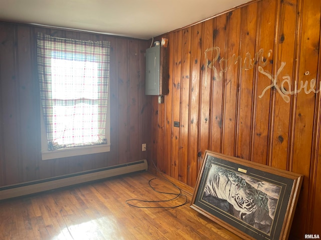 unfurnished room featuring a healthy amount of sunlight, wood-type flooring, baseboard heating, and electric panel