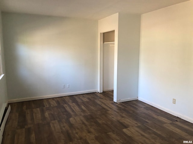 empty room with dark hardwood / wood-style flooring and a baseboard heating unit