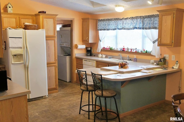 kitchen featuring a kitchen bar, stacked washing maching and dryer, a textured ceiling, white appliances, and sink