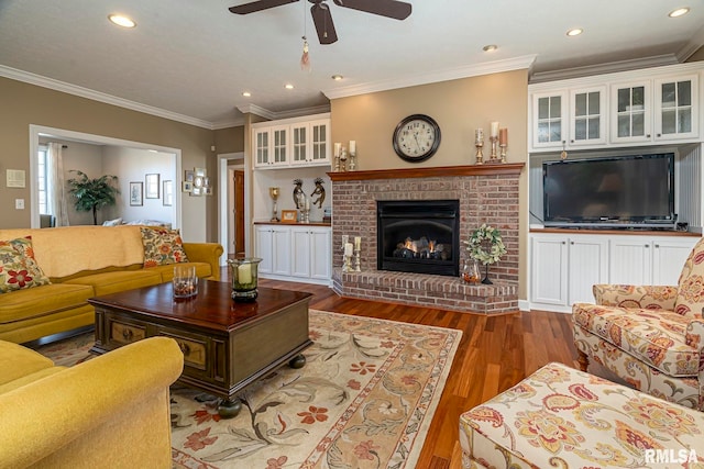 living room featuring crown molding, ceiling fan, wood-type flooring, and a brick fireplace