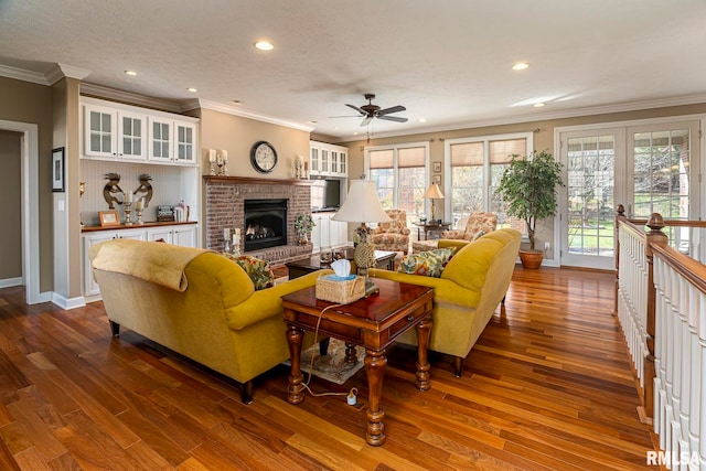 living room featuring ceiling fan, a brick fireplace, a textured ceiling, hardwood / wood-style flooring, and ornamental molding