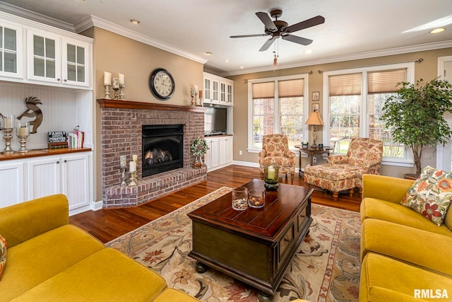 living room featuring wood-type flooring, a brick fireplace, ceiling fan, and crown molding