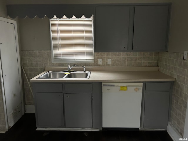 kitchen with white dishwasher, gray cabinetry, sink, and tile walls