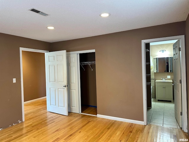 unfurnished bedroom with connected bathroom, sink, a textured ceiling, a closet, and light wood-type flooring