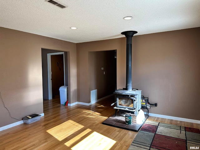 living room with hardwood / wood-style floors, a wood stove, and a textured ceiling