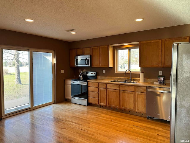 kitchen with a textured ceiling, light hardwood / wood-style floors, sink, and stainless steel appliances