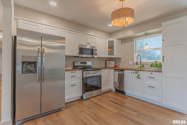 kitchen with pendant lighting, light wood-type flooring, white cabinetry, and appliances with stainless steel finishes