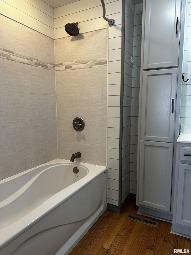 bathroom featuring wooden walls, hardwood / wood-style floors, and tiled shower / bath combo