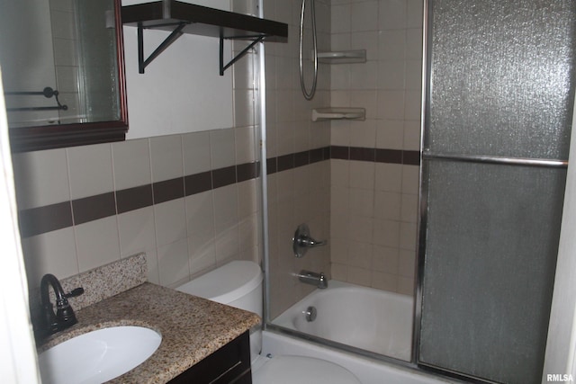 full bathroom with combined bath / shower with glass door, vanity, toilet, and tile walls