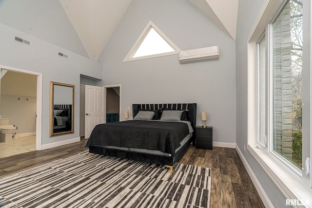 bedroom featuring an AC wall unit, multiple windows, ensuite bath, and dark wood-type flooring