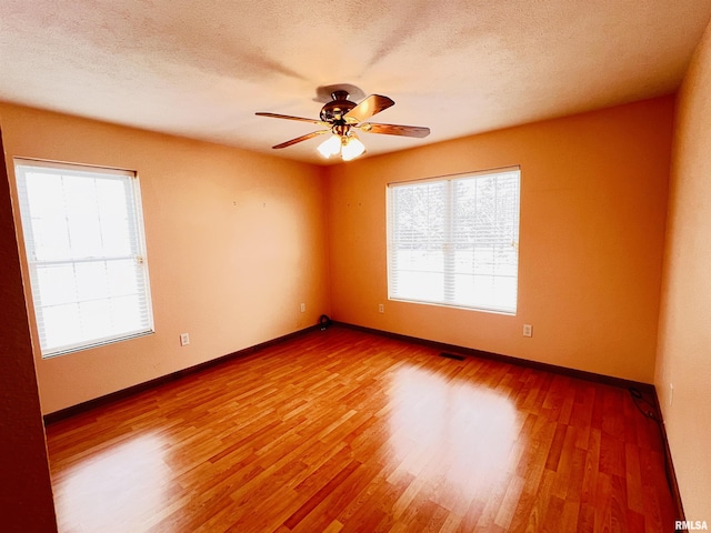 spare room with a textured ceiling, hardwood / wood-style flooring, ceiling fan, and a healthy amount of sunlight