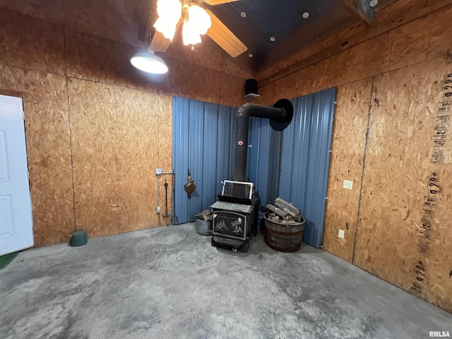 interior space featuring ceiling fan, a wood stove, concrete flooring, and vaulted ceiling