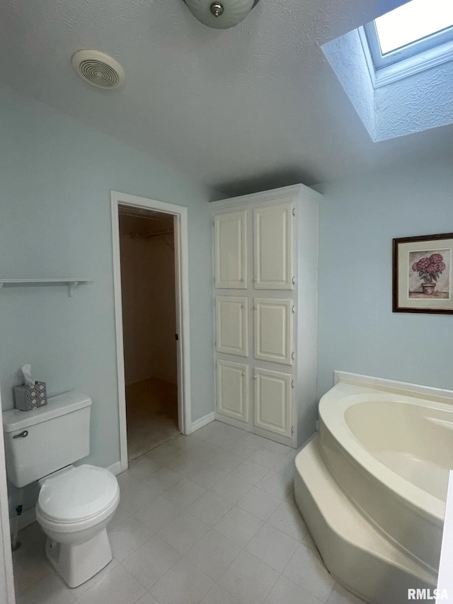 bathroom with tile patterned floors, a tub, lofted ceiling with skylight, and toilet