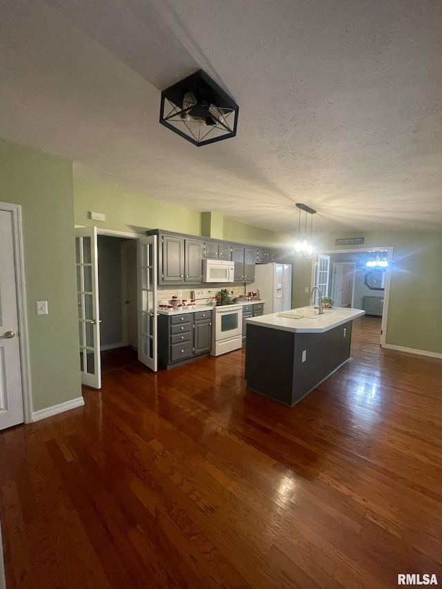 kitchen with dark wood-type flooring, an island with sink, a textured ceiling, white appliances, and gray cabinets