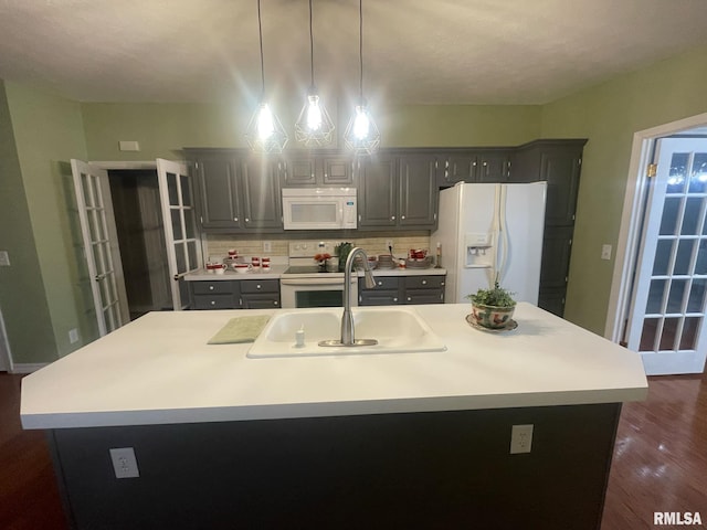 kitchen featuring white appliances, decorative light fixtures, a kitchen island with sink, and sink