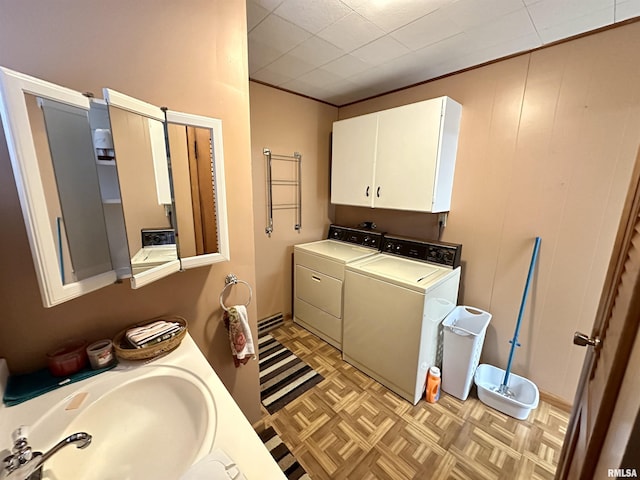 laundry area featuring washing machine and dryer, sink, light parquet flooring, and cabinets