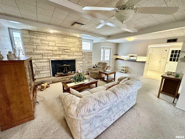 living room with beam ceiling, ceiling fan, a fireplace, and light colored carpet