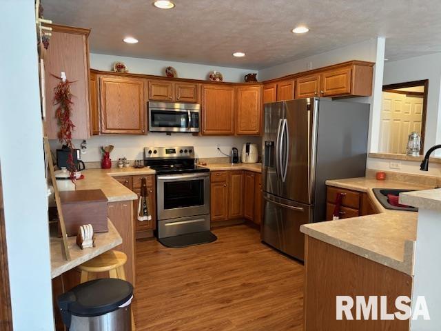 kitchen with sink, light hardwood / wood-style flooring, appliances with stainless steel finishes, a kitchen bar, and kitchen peninsula