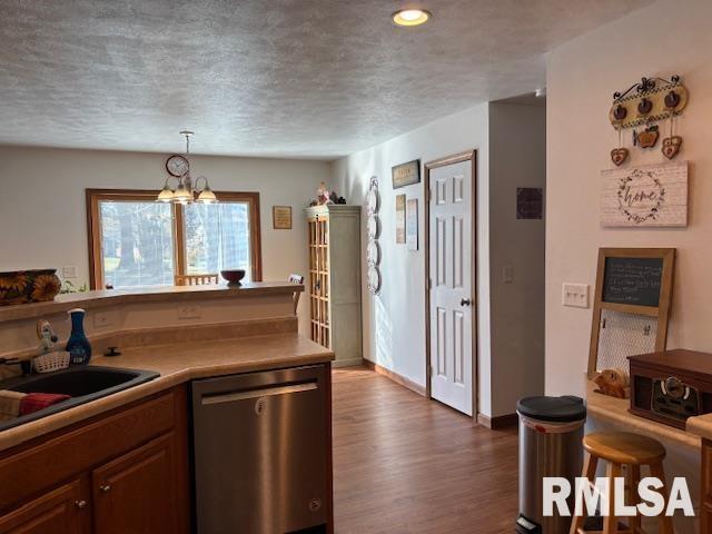 kitchen with stainless steel dishwasher, dark wood-type flooring, sink, a chandelier, and hanging light fixtures