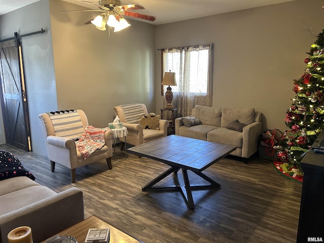 living room with ceiling fan, a barn door, and dark wood-type flooring