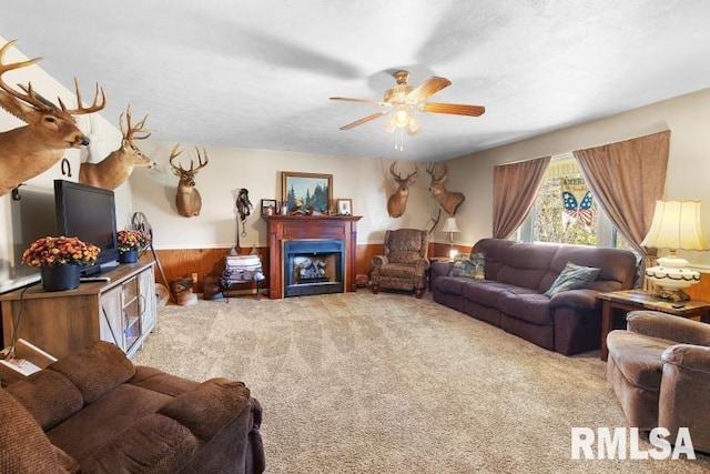 carpeted living room with ceiling fan and wood walls