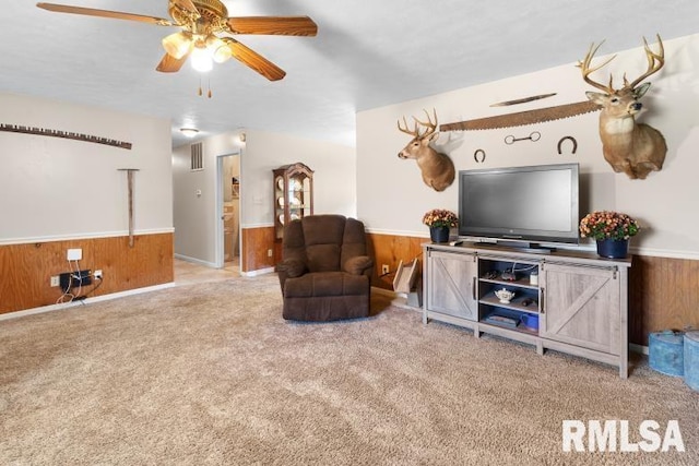 living room with wooden walls, ceiling fan, and light carpet