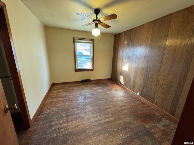 unfurnished room featuring wooden walls, ceiling fan, and dark wood-type flooring