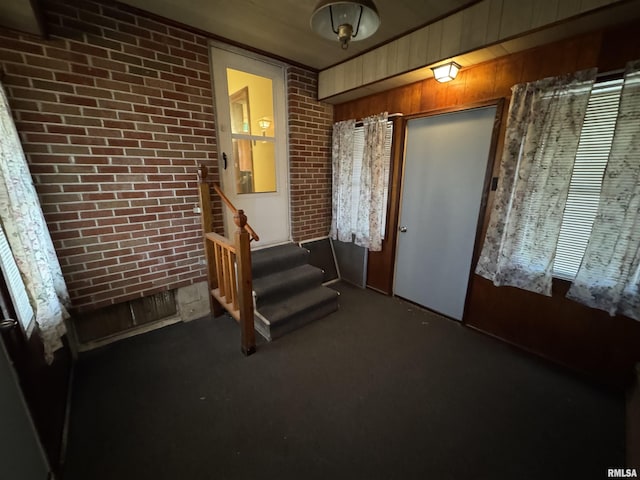 interior space with wood walls, brick wall, and dark colored carpet