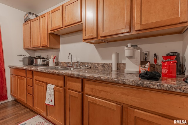 kitchen featuring dark stone countertops, sink, and light hardwood / wood-style flooring