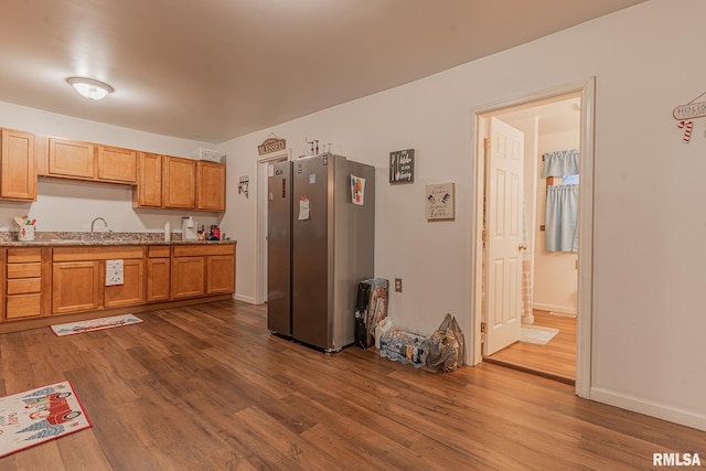 kitchen with dark hardwood / wood-style floors, stainless steel fridge, light stone counters, and sink