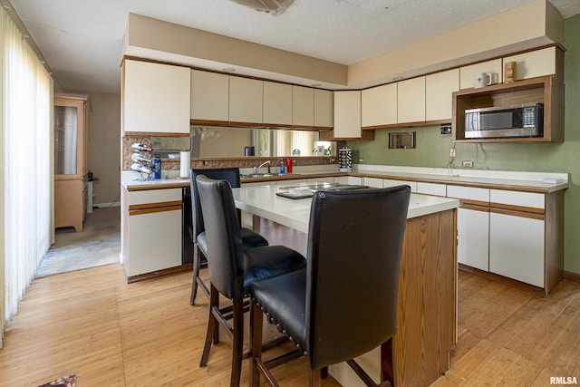 kitchen featuring a textured ceiling, sink, light hardwood / wood-style flooring, a kitchen island, and stainless steel microwave