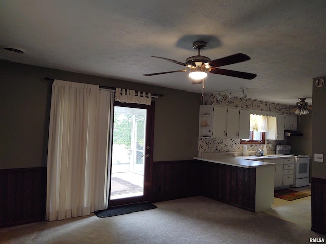 kitchen with kitchen peninsula, light colored carpet, wooden walls, white cabinets, and white range with electric cooktop