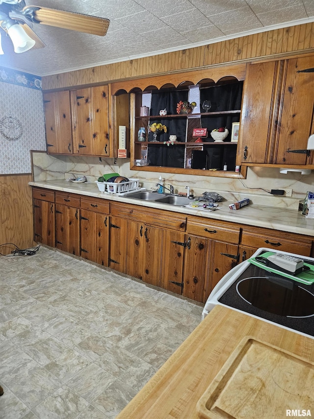 kitchen featuring ceiling fan, stove, sink, and wooden walls